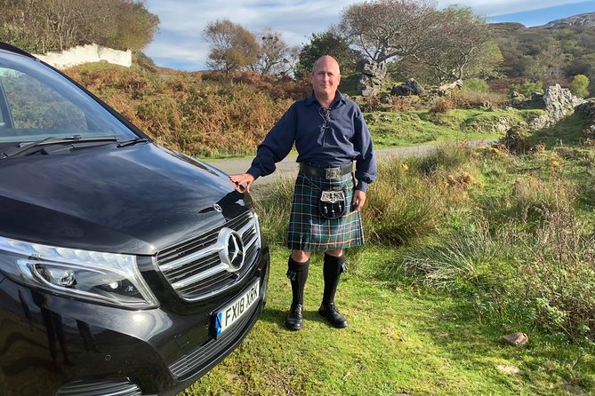 A tour guide stands proudly in Pitlochry, ready to unveil the treasures of the Highlands, his enthusiasm matching the majestic backdrop of rolling hills and verdant forests, promising an unforgettable journey through Scotland's heartland.